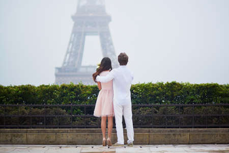 Beautiful romantic couple in love looking at the Eiffel tower in Paris on a cloudy and foggy rainy day, back viewの写真素材