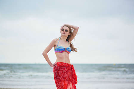 Beautiful young woman in bikini and red pareo on the sand on beach, relaxing and sunbathing. Summer vacations conceptの写真素材