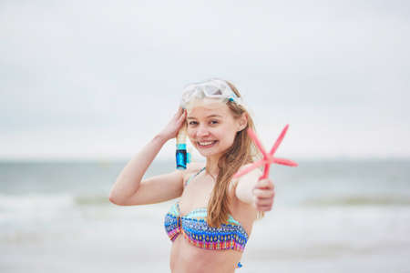Happy young woman in bikini with snorkelling equipment and pink starfish enjoying summer vacation holidays by ocean or sea. Beach, travelling and people conceptの写真素材