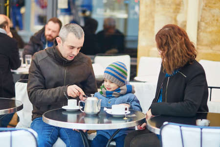 Happy family of three, father, mother and their adorable little son, spending time together in cafe...