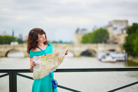 Young woman on Pont des Arts, pedestrian bridge over the Seine, using map and planning her itinerary in Paris, Franceの写真素材