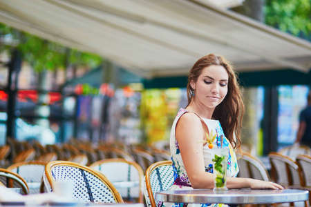 Smiling French woman sitting on the open terrace of Parisian cafe with cocktail on a summer dayの写真素材