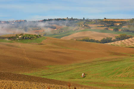 Scenic view of Tuscan fields and hills with fog at early morning. Val d'Orcia, Tuscany, Italy