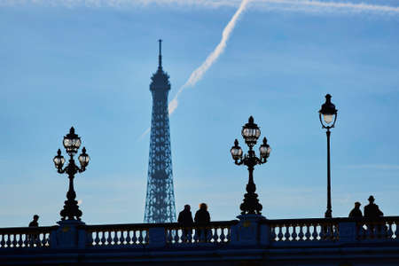 Scenic cityscape of Paris with silhouettes of people and lanterns on the famous Alexandre III bridge and the Eiffel tower over the blue skyの写真素材