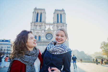 Two young girls walking together in Paris near Notre-Dame cathedral. Tourism or friendship concept