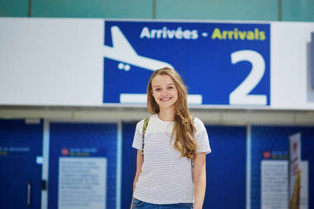 Beautiful young tourist girl with backpack and carry on luggage in international airport, at arrivals doorの写真素材