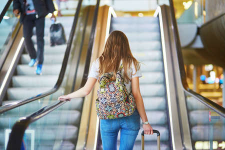 Beautiful young tourist girl with backpack and carry on luggage in international airport, on...