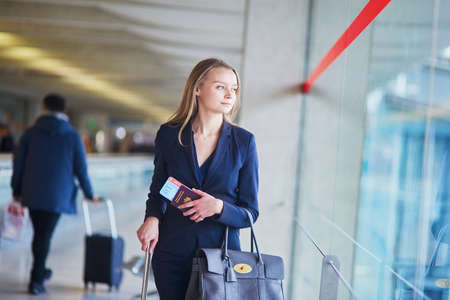 Young elegant business woman with hand luggage looking through the window in international airport terminal, waiting for her flightの写真素材