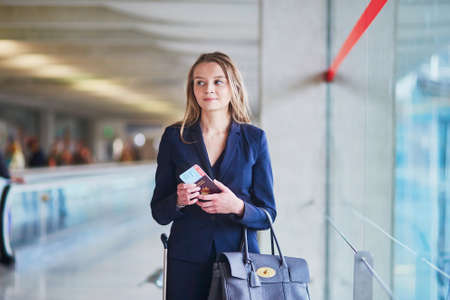 Young elegant business woman with hand luggage looking through the window in international airport terminal, waiting for her flightの写真素材