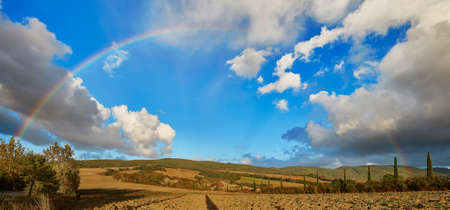 Scenic panorama of Tuscany countryside with full rainbow over the blue sky at rainy weatherの写真素材