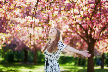Beautiful young woman enjoying sunny day in park during cherry blossom season on a nice spring dayの写真素材