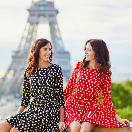 Beautiful twin sisters in red and black polka dot dresses in front of the Eiffel tower in Paris, Franceの写真素材