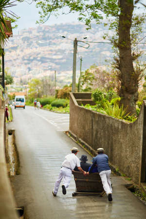 Famous fun tourist activity in Funchal, Madeira island, Portugal. Toboggan riders pushing wooden sledge with tourists downhill with high speedの写真素材