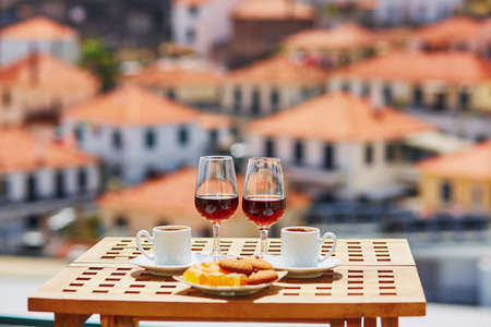 Two glasses of Madeira wine, two cups of fresh espresso coffee and traditional Portuguese sweets in cafe with view to Funchal town, Madeira, Portugalの写真素材