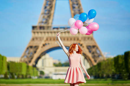 Beautiful young woman in pink dress with bunch of balloons dancing near the Eiffel tower in Paris, Franceの写真素材