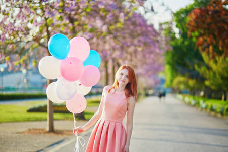 Beautiful young woman in pink dress with bunch of balloons in Parisの写真素材