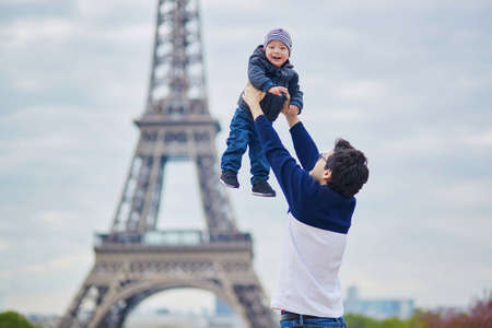 Father throwing his little son in the air near the Eiffel tower in Paris. Happy family of two enjoying their vacation in France.の写真素材