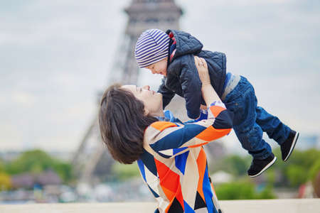 Mother throwing her little son in the air near the Eiffel tower in Paris. Happy family of two enjoying their vacation in France.の写真素材