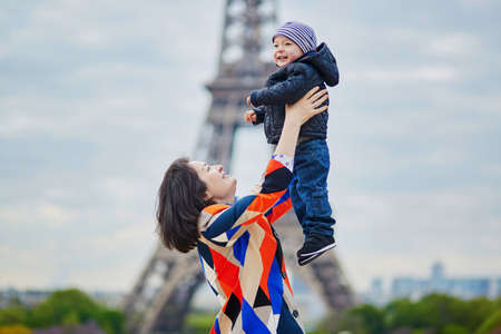 Mother throwing her little son in the air near the Eiffel tower in Paris. Happy family of two enjoying their vacation in France.の写真素材