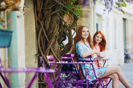 Two Parisian women drinking coffee together in an outdoor cafe with wisteria in full bloom. Paris, Franceの写真素材