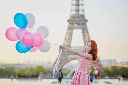 Happy young girl with bunch of pink and blue balloons in front of the Eiffel tower in Paris, France