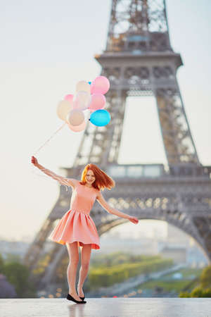 Happy young girl with bunch of pink and blue balloons in front of the Eiffel tower in Paris, France