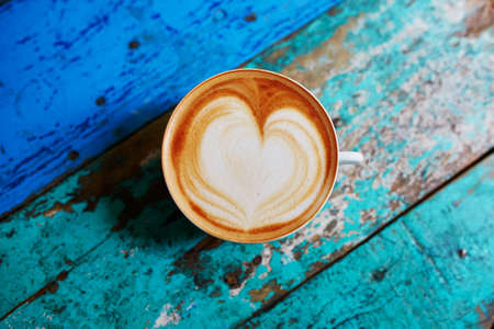 Cup of fresh coffee with heart form milk drawing on blue wooden table, view from above, flat layの写真素材