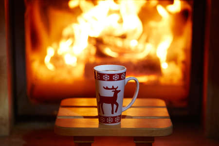 Cup of hot chocolate and marshmallows near fireplace with many candles. Cozy romantic Christmas eveningの写真素材