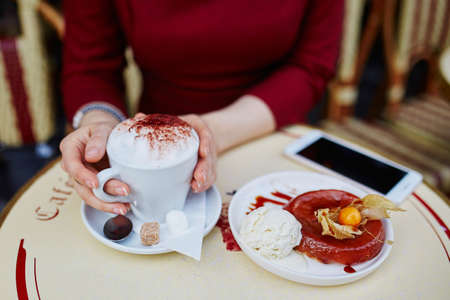 Closeup of woman's hands with mobile phone, cup of coffee and cake in Parisian outdoor cafeの写真素材