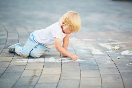 Adorable little boy drawing with colorful chalks on asphalt. Summer activity and creative games for small kidsの写真素材