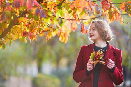 Beautiful young woman with bunch of colorful autumn leaves walking in park on a fall dayの写真素材
