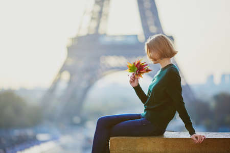 Beautiful young French woman with bunch of colorful autumn leaves near the Eiffel tower in Paris on a fall dayの写真素材