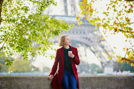 Beautiful young French woman with bunch of colorful autumn leaves near the Eiffel tower in Paris on a fall dayの写真素材