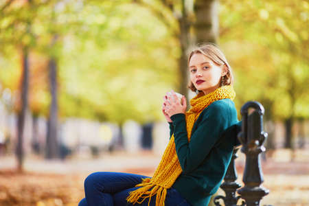 Happy young girl in yellow scarf with coffee to go walking in autumn park on a bright fall dayの写真素材