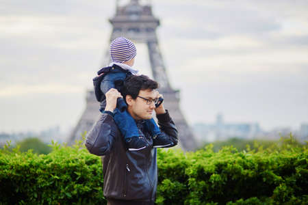 Father holding his little son on his shoulders near the Eiffel tower in Paris. Happy family of two enjoying their vacation in France.の写真素材