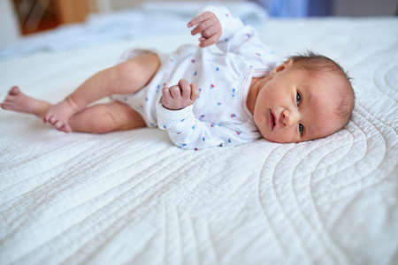 Adorable newborn baby girl lying on her parents' bed at home