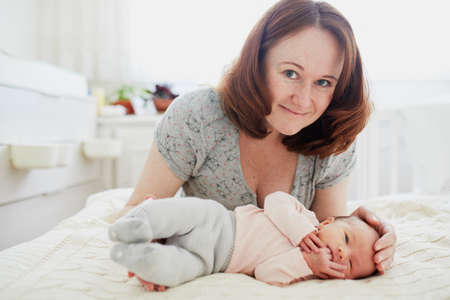 Beautiful woman with her adorable newborn baby girl. Mother and daughter together in bedroomの写真素材