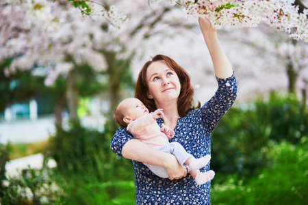 Happy young mother with her 2 months baby girl enjoying cherry blossom season on a spring day