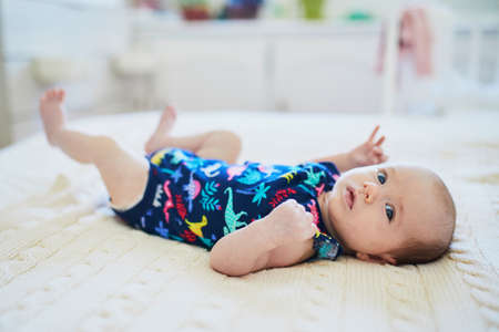 Adorable two months baby girl relaxing in bedroom on knitted blanket on a sunny morning