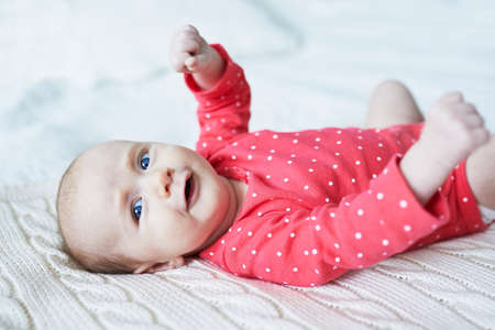Adorable two months baby girl relaxing in bedroom on knitted blanket on a sunny morning