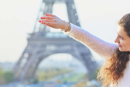 Happy young woman near the Eiffel tower in Paris, France. Tourist showing her bracelet with mini Eiffel towerの写真素材