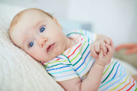 Adorable blue eyed 3 months old baby girl in colorful clothes at homeの写真素材