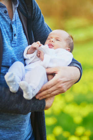 Father holding 4 weeks old baby girl in his arms. 1 month old child in dad's hands outdoors. First walk for a newbornの写真素材