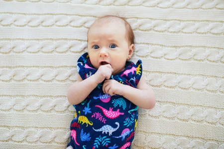 Surprised 1 month old baby girl lying on knitted blanket. Emotions and face expressions of a newbornの写真素材
