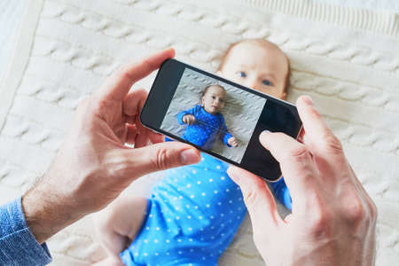 Father taking a photo of his newborn baby with mobile phoneの写真素材