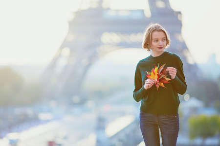 Beautiful young French woman with bunch of colorful autumn leaves near the Eiffel tower in Paris on a fall dayの写真素材