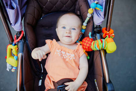 Baby girl with colorful toys in stroller. Little child in pram. Infant kid outdoors