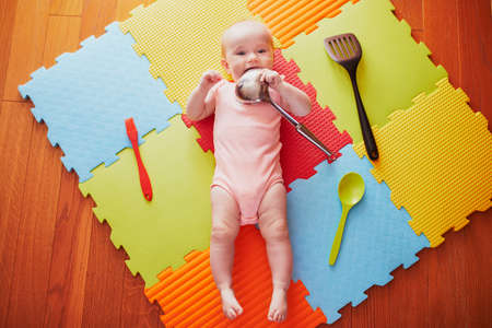 Baby girl with kitchen utensils. Little child lying playmat and playing with kitchenware. Real things as toys for children. Infant kid in sunny nursery.の写真素材