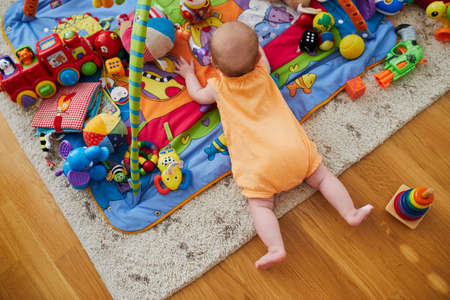 Baby girl with many colorful toys. Little child lying on playmat. Infant kid in nursery.の写真素材