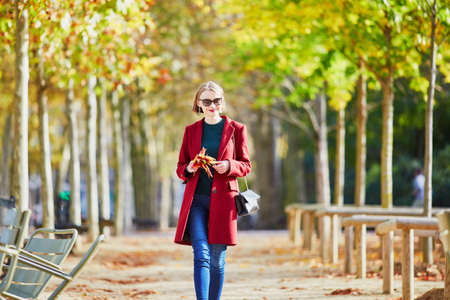 Beautiful young woman with bunch of colorful autumn leaves walking in park on a fall day. Luxembourg garden, Paris, Franceの写真素材